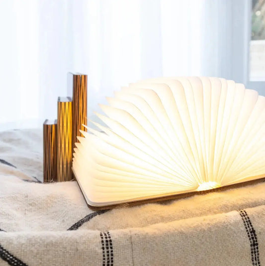 Glowbook Lamp - Foldable Wooden Light open on a blanket, emitting a warm glow with sculptural pages, ideal for cozy home lighting decor.